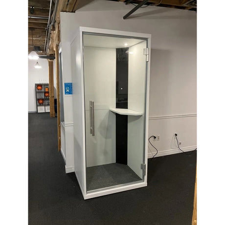 Cabine acoustique OneZone blanche avec intérieur noir, installée dans un espace bureau avec plafond ouvert