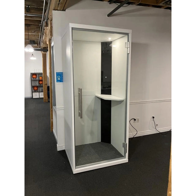 Cabine acoustique OneZone blanche avec intérieur noir, installée dans un espace bureau avec plafond ouvert