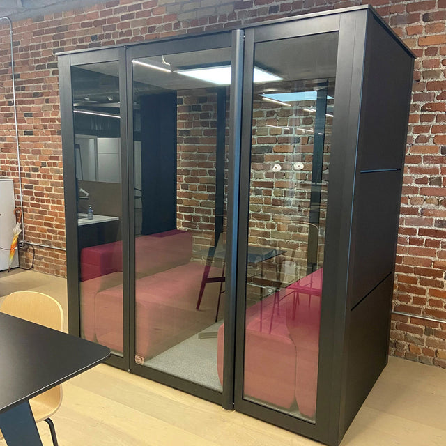 Cabine Island 4B noire avec banquettes rouges, installée dans un bureau en briques apparentes