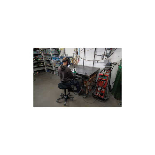 Person welding at a workbench while seated on a Synetik Omnistool Welding stool.