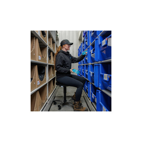 Personne assise sur un tabouret Synetik Omnistool Vinyle pour prendre des pièces dans des bacs de rangement.