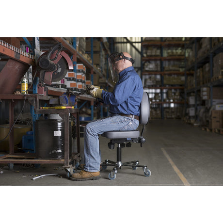 Personne assise sur une chaise Synetik SF180 en vinyle à un établi dans un atelier industriel.