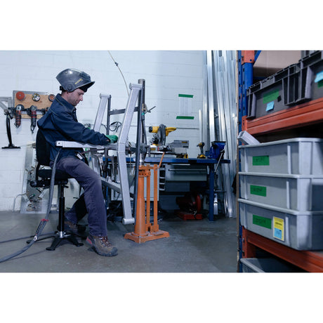 Personne utilisant un siège assis-debout Synetik TA190 Soudure pour travailler sur une pièce métallique dans un atelier.