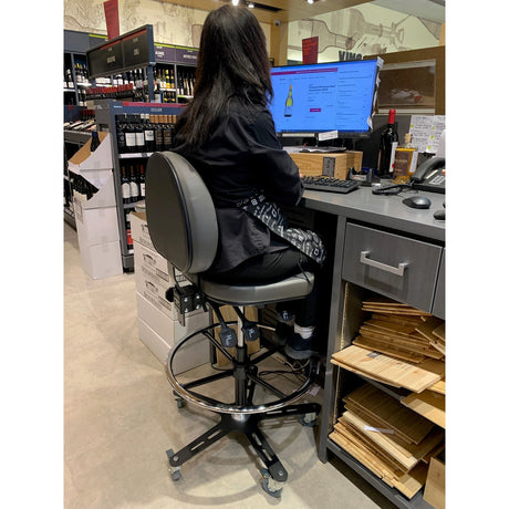 Chaise haute Synetik TF180 en vinyle utilisée à un comptoir de commerce, vue arrière avec dossier et anneau repose-pieds.